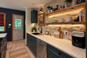 Una cocina con salpicadero de piedra, estantes de madera y lavavajillas empotrado.