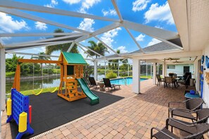 A covered outdoor area with a children's play structure, a pool, and outdoor seating.