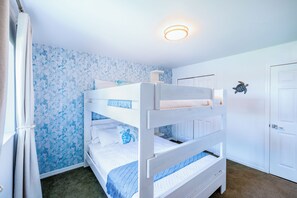 A bunk bed room with a ceiling light fixture, a door, and a wall with a marine-themed wallpaper.