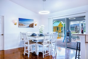 A dining area with a white table set for four, white chairs, and a painting of a beach scene.