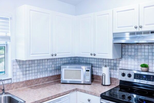 Une cuisine moderne avec des meubles blancs, un four à micro-ondes, une cuisinière et une petite plante en pot.