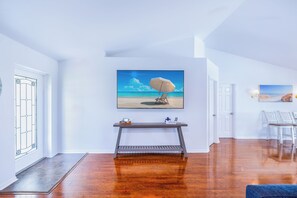 A modern living room with a wooden floor, a console table with a painting, and a door with a glass panel.