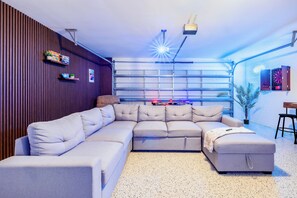 A modern living room with a sectional sofa, a dartboard, and a mounted shelf with books and games.