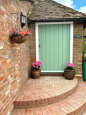 A brick building with a green door, a hanging flower basket, and two potted plants.