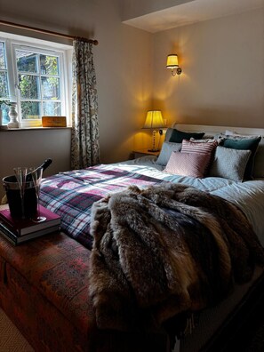 A bedroom with a bed, a bedside table with a lamp, a window with curtains, and a bottle of Veuve Clicquot on the table.