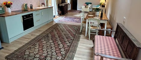 A spacious loft with exposed wooden beams, a kitchen with light blue cabinets, a dining area with a checkered table, and a large patterned rug.