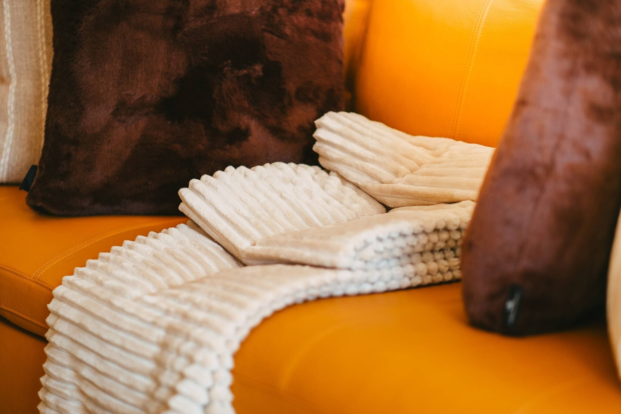 Un canapé agrémenté d’un plaid blanc à texture et d’un coussin marron foncé.