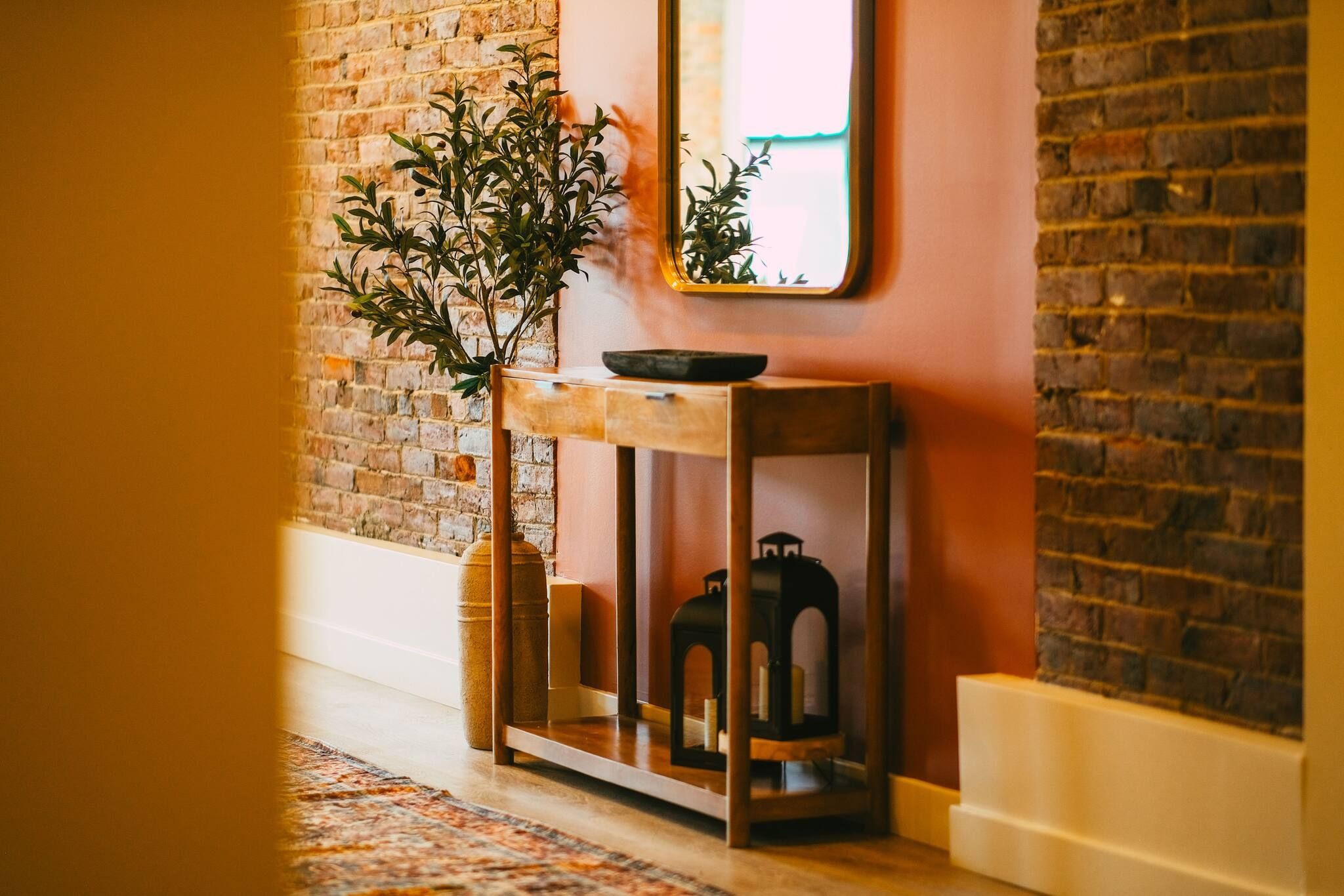 A hallway with a brick wall, a wooden bench with a plant, and a lantern.