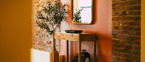 A hallway with a brick wall, a wooden bench with a plant, and a lantern.