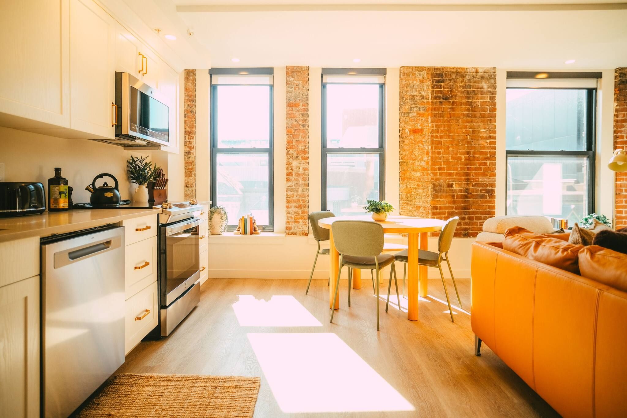 Eine moderne Küche mit Edelstahlgeräten, ein Essbereich mit Ziegelwand und ein gemütliches orangefarbenes Sofa.