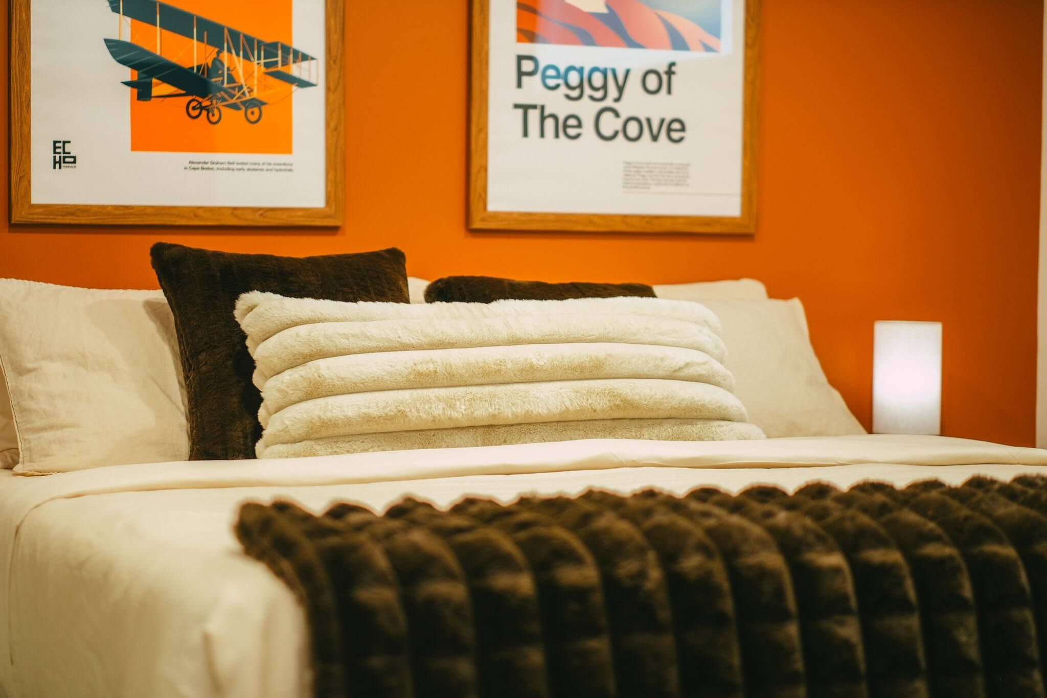 A neatly made bed with white linens and a brown throw blanket, accompanied by two pillows, one white and one brown.