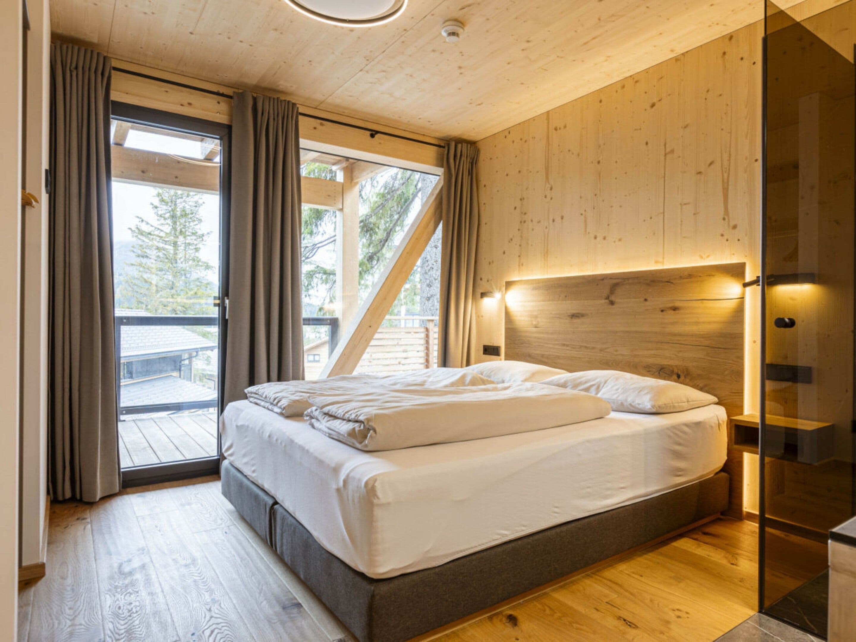 A bedroom with a bed, wooden walls, a glass door, and a view of the outdoors.