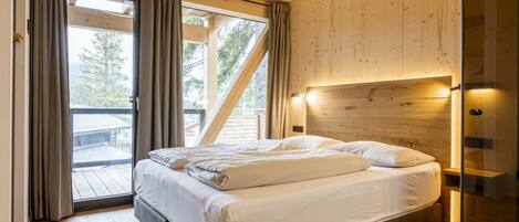A bedroom with a bed, wooden walls, a glass door, and a view of the outdoors.