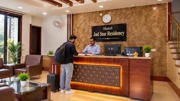 A hotel reception desk with a sign reading 'Hotel Jad Star Residency,' a reception area with seating, and a clock on the wall.