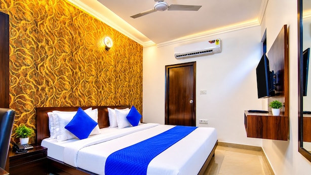 A hotel room with a bed, a ceiling fan, an air conditioning unit, a TV, and a wooden door. - HOTEL JAD STAR RESIDENCY (New Delhi)