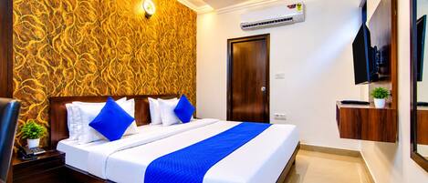 A hotel room with a bed, a ceiling fan, an air conditioning unit, a TV, and a wooden door.