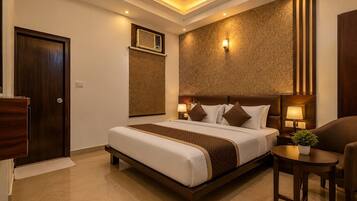 A hotel room with a large bed, bedside lamps, a small table with a plant, and a wall-mounted air conditioning unit.