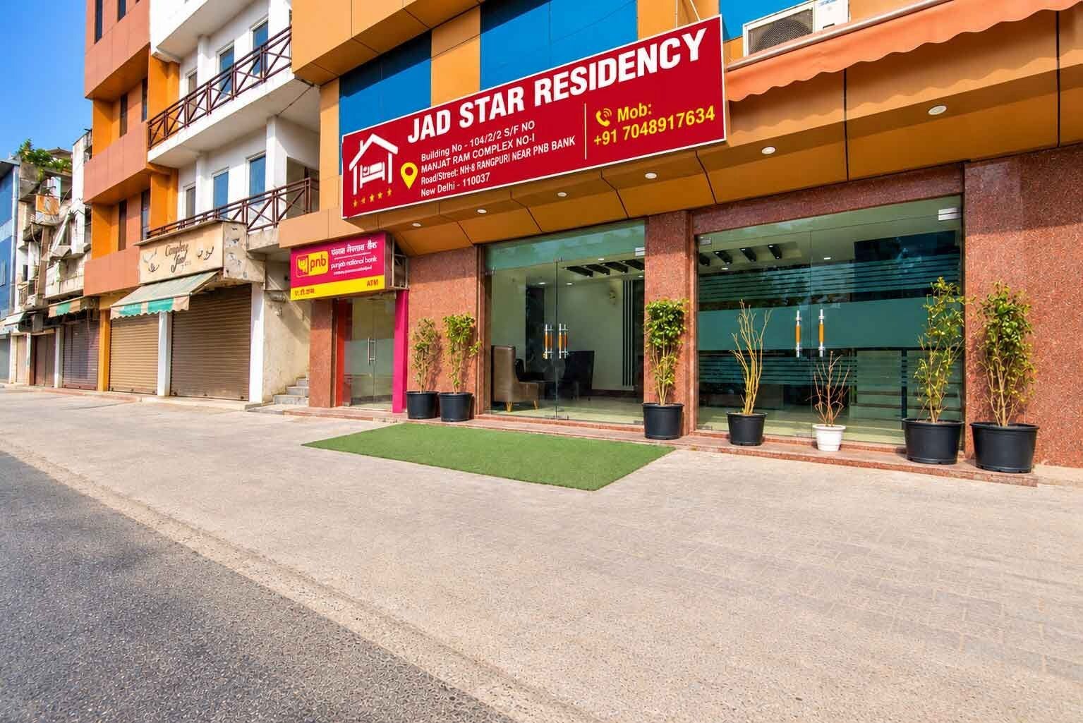 A building with a sign for JAD STAR RESIDENCY, an ATM, and potted plants in front.