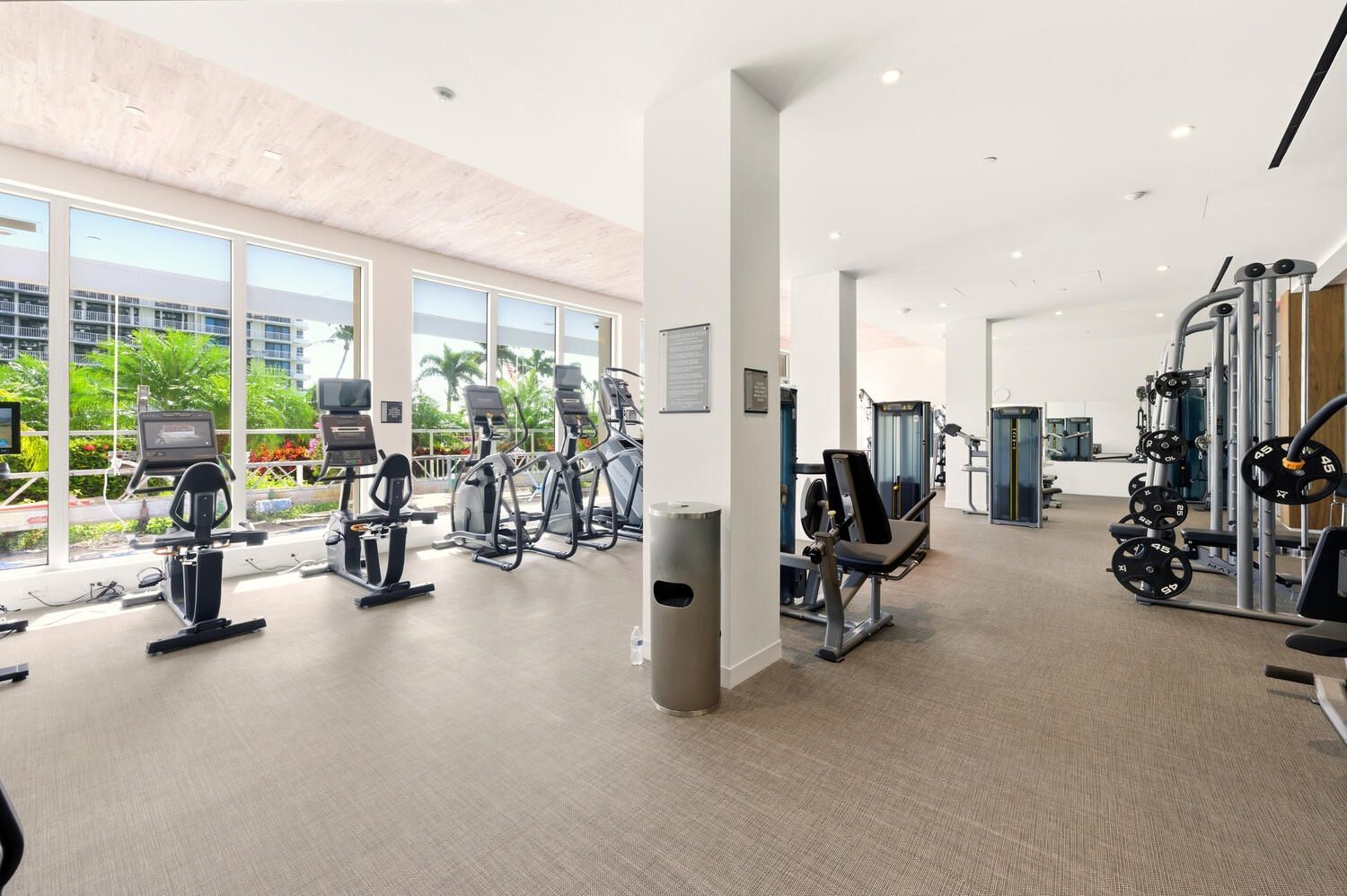 Une salle de sport moderne équipée de machines de cardio, de matériel de musculation et de grandes fenêtres donnant sur un espace verdoyant.