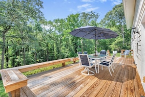 Een houten terras met een tafel, stoelen, een parasol en een bank.