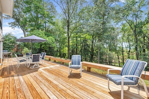 Een houten terras met tuinmeubilair, waaronder stoelen, een tafel en een barbecue.