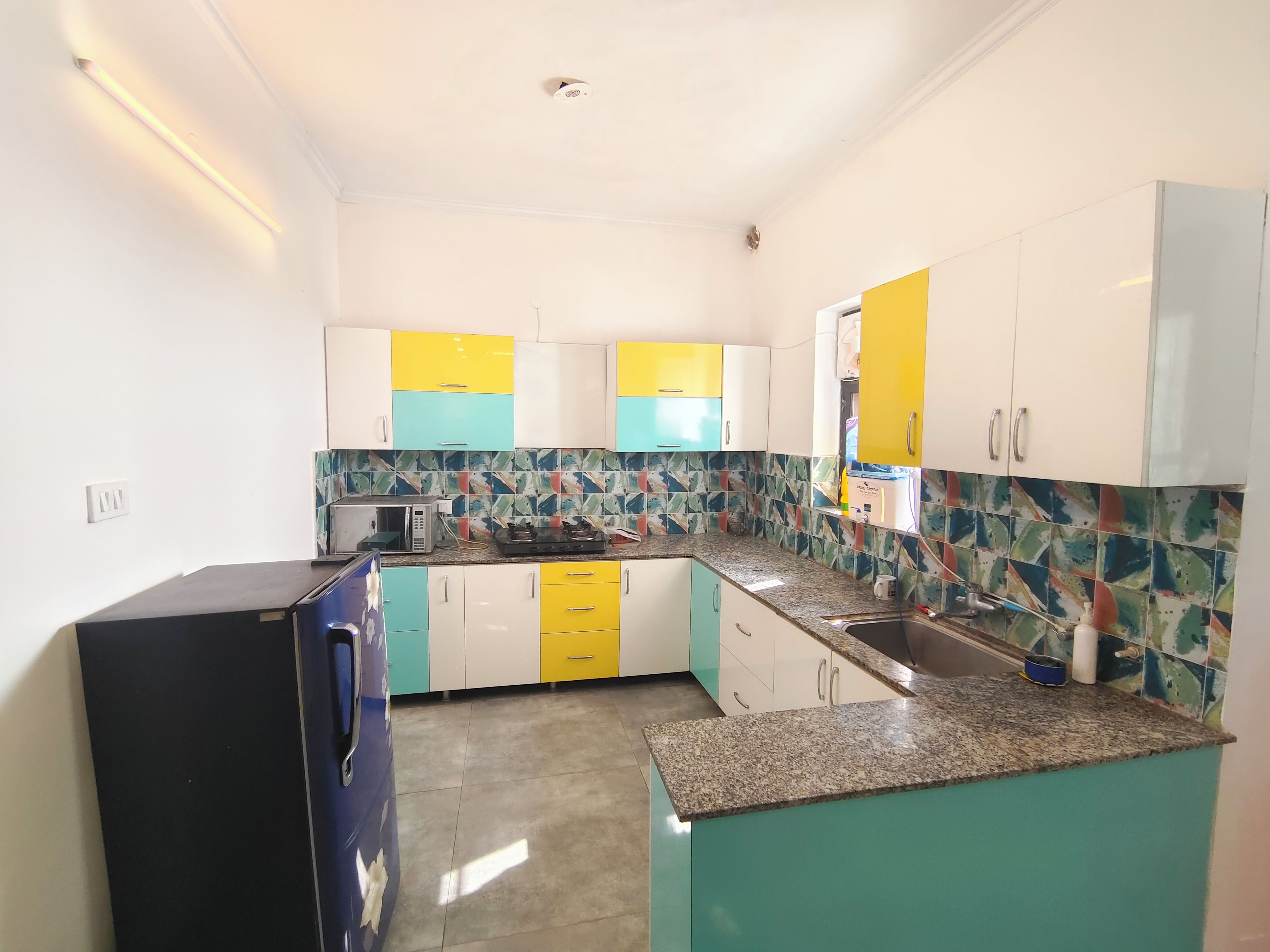 A kitchen with teal and yellow cabinets, a microwave, a gas stove, and a sink.