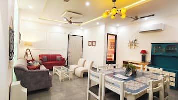 A modern living room with a red sofa, white armchairs, a glass coffee table, and a dining area with a blue table and white chairs.