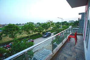 A balcony with a view of a road and greenery, a red chair, and a table. - Eden Villa (Kharar)