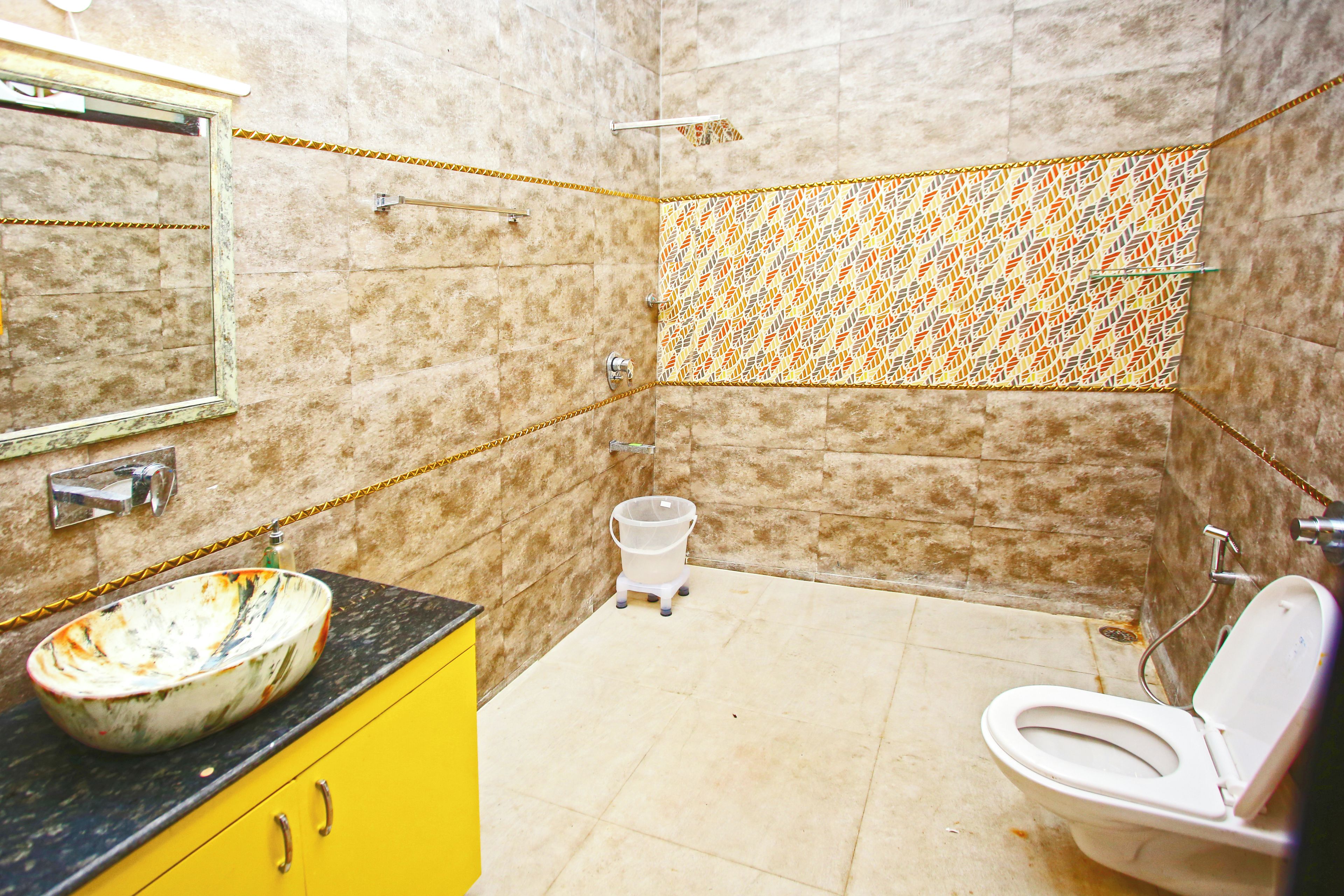 A bathroom with a marble wall, a yellow vanity, a white sink, a toilet, and a shower area.