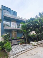 Un edificio residencial de dos pisos con un balcón, plantas en macetas y una valla de piquete blanca.