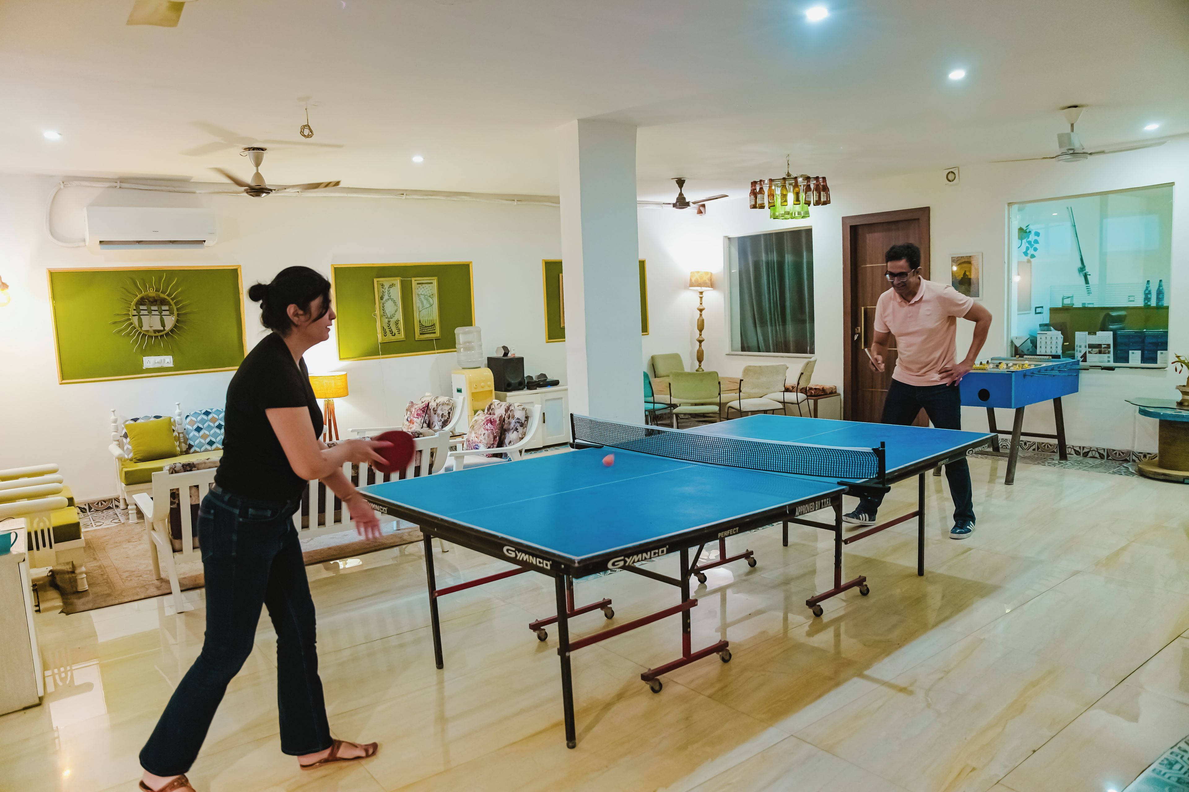 Una stanza con tavolo da ping pong, sedie e un giocatore di tennis tavolo.