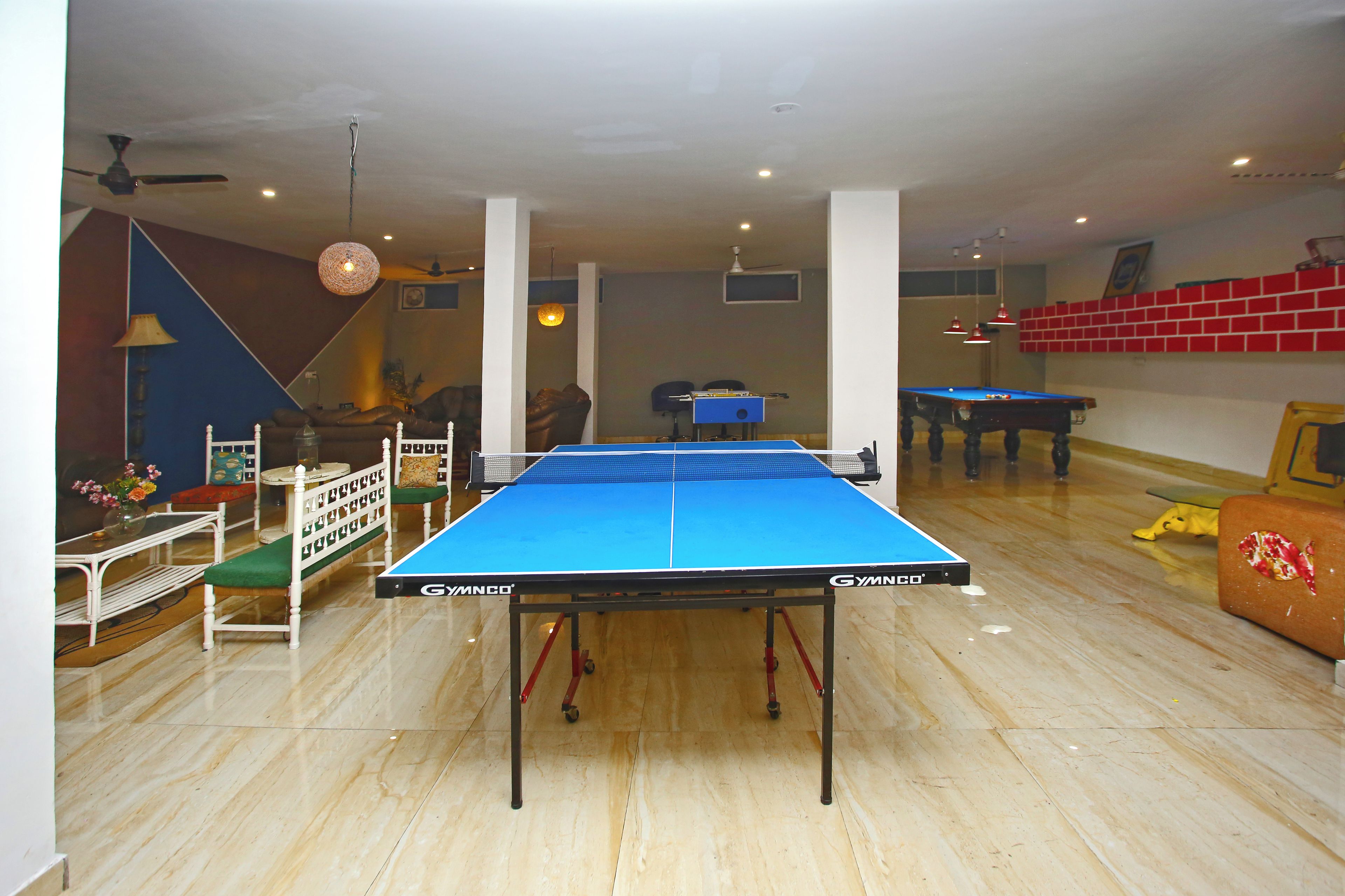 Uma sala de bilhar com mesa azul, mesa de pebolim e mesa de sinuca.