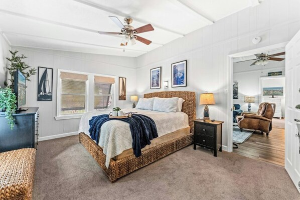 Een slaapkamer met een bed, nachtkastjes, een plafondventilator en uitzicht op een andere kamer.