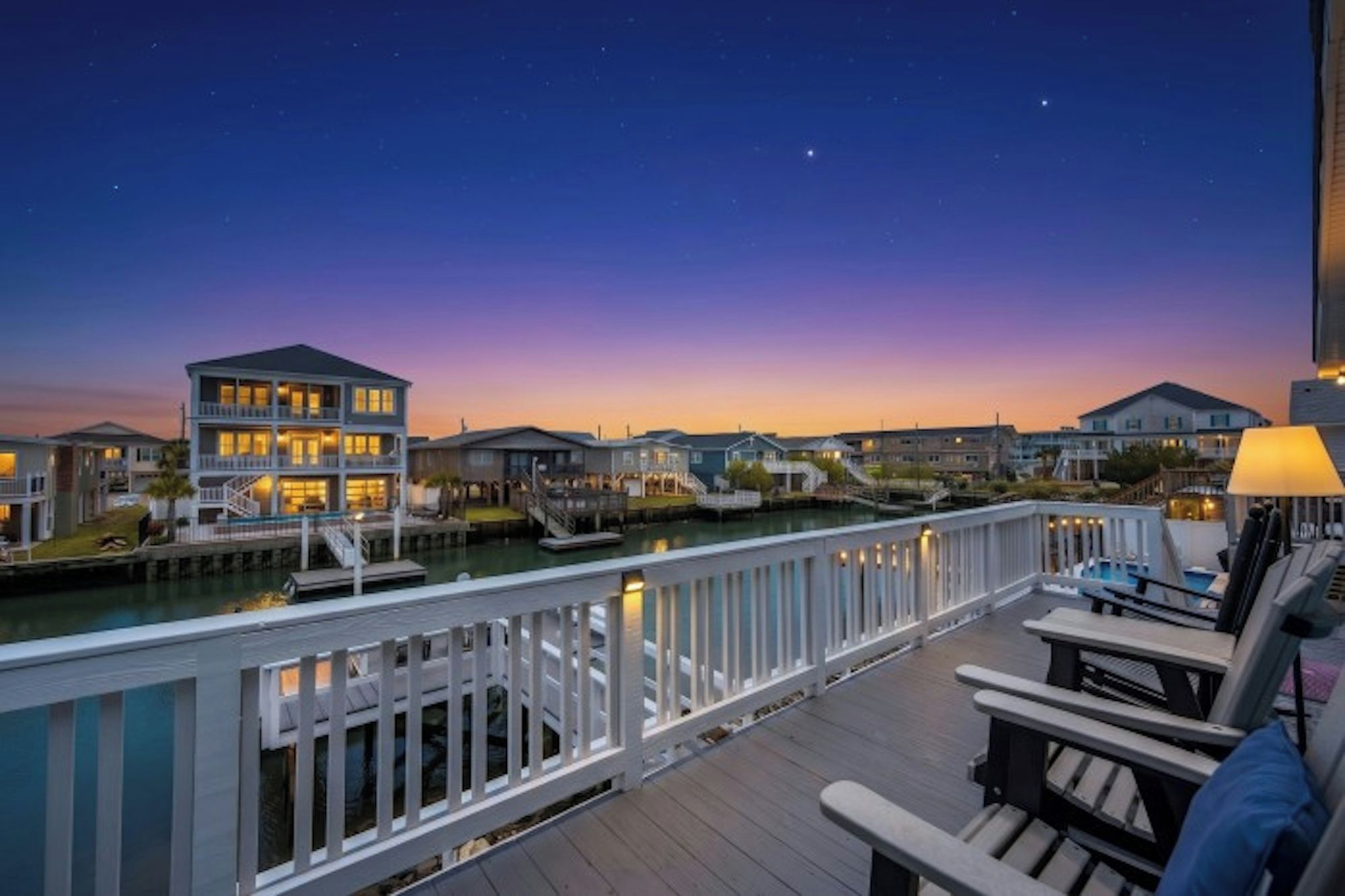 A waterfront property with a dock, a wooden deck, and a view of the water at dusk.