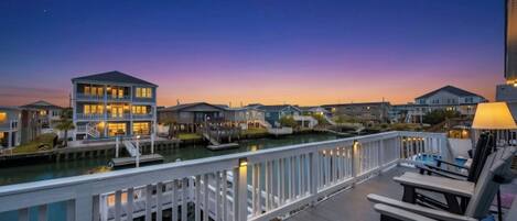 A waterfront property with a dock, a wooden deck, and a view of the water at dusk.