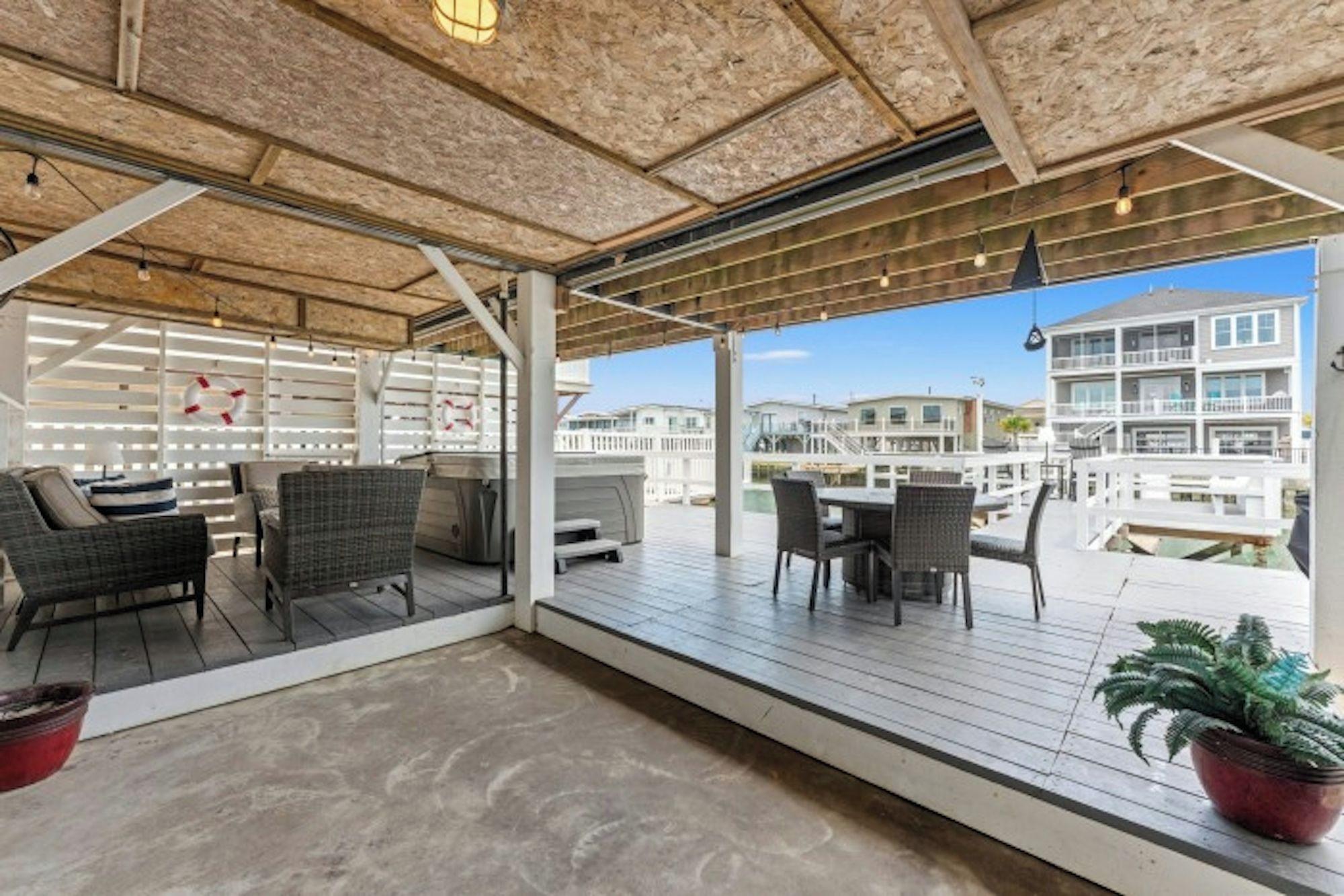 An outdoor patio with wicker furniture, a hot tub, and a view of a residential area.