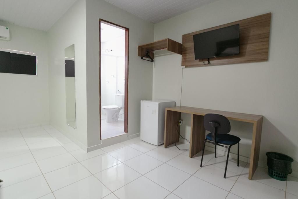 A room with a desk, chair, television, and a refrigerator.