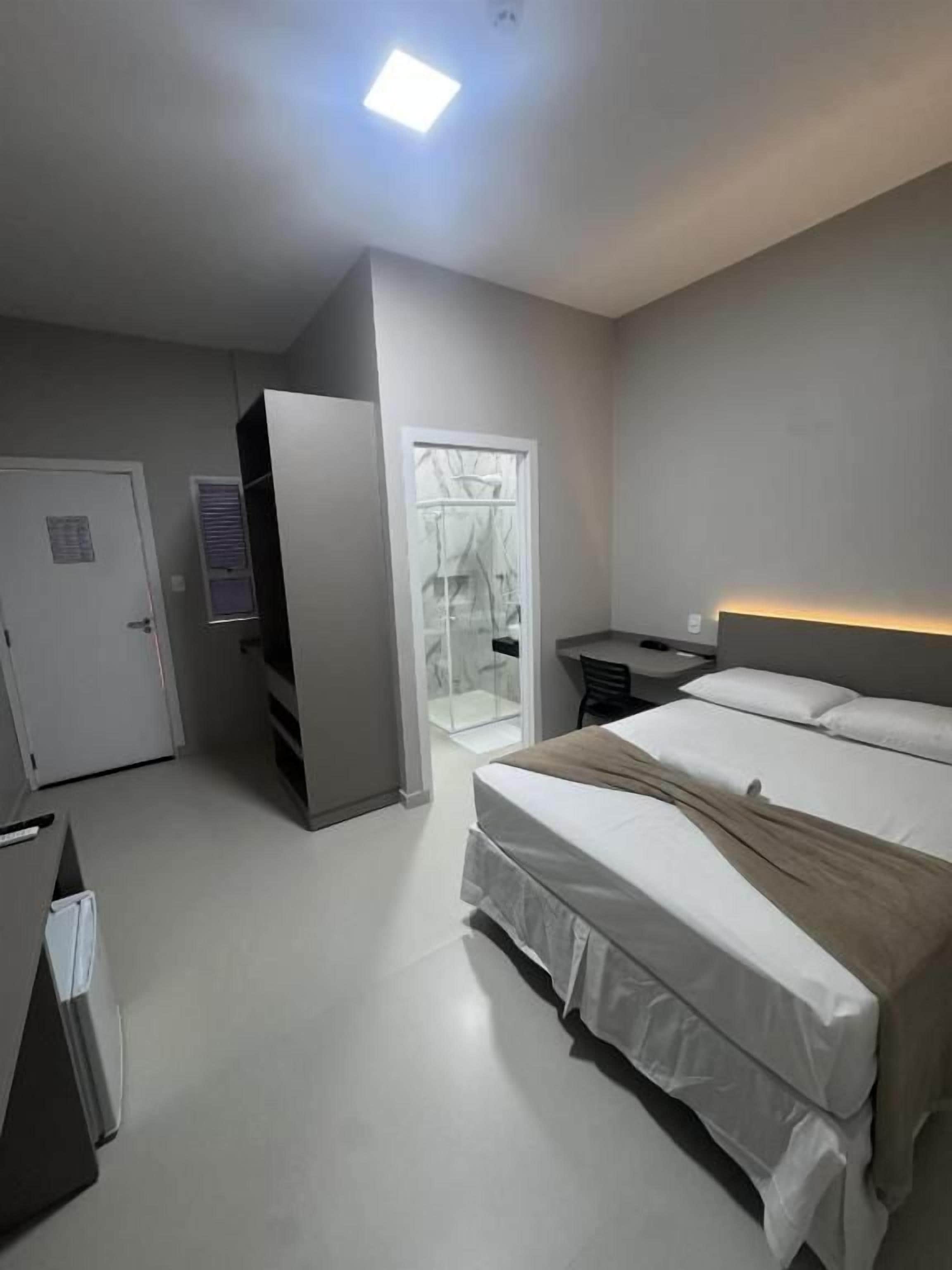 Quarto de hotel com cama, mesa de cabeceira e guarda-roupa.