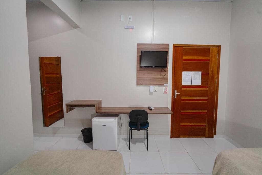 A room with a bed, a desk, a chair, a television mounted on the wall, and a small refrigerator.