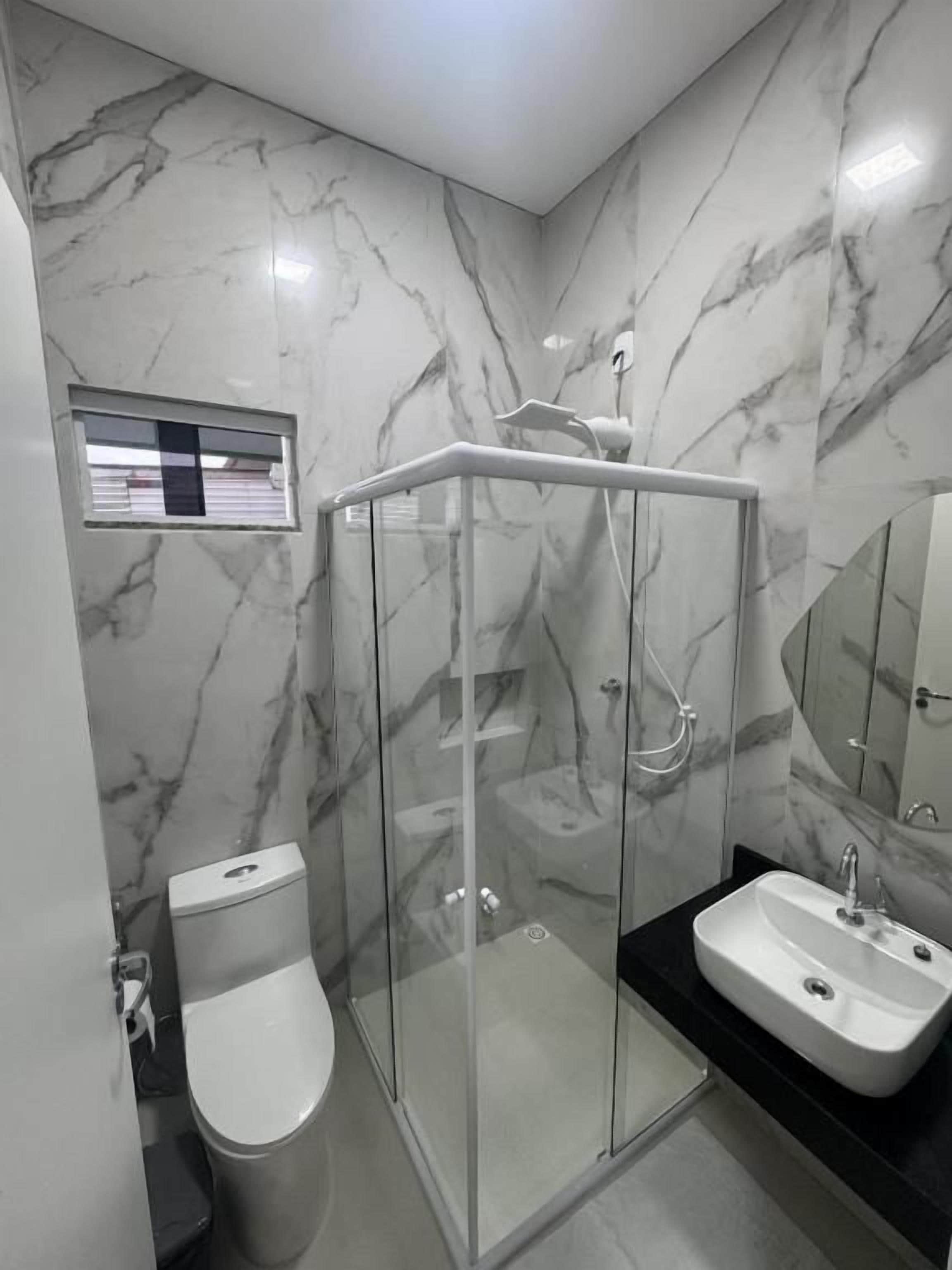 Um banheiro moderno com chuveiro em vidro, vaso sanitário e pia.