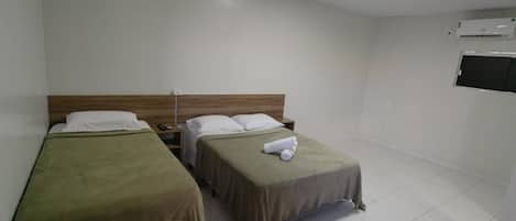 A hotel room with two single beds, a wooden headboard, a flat-screen TV, and an air conditioning unit.