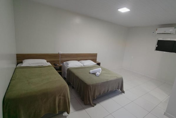A hotel room with two single beds, a wooden headboard, a flat-screen TV, and an air conditioning unit.