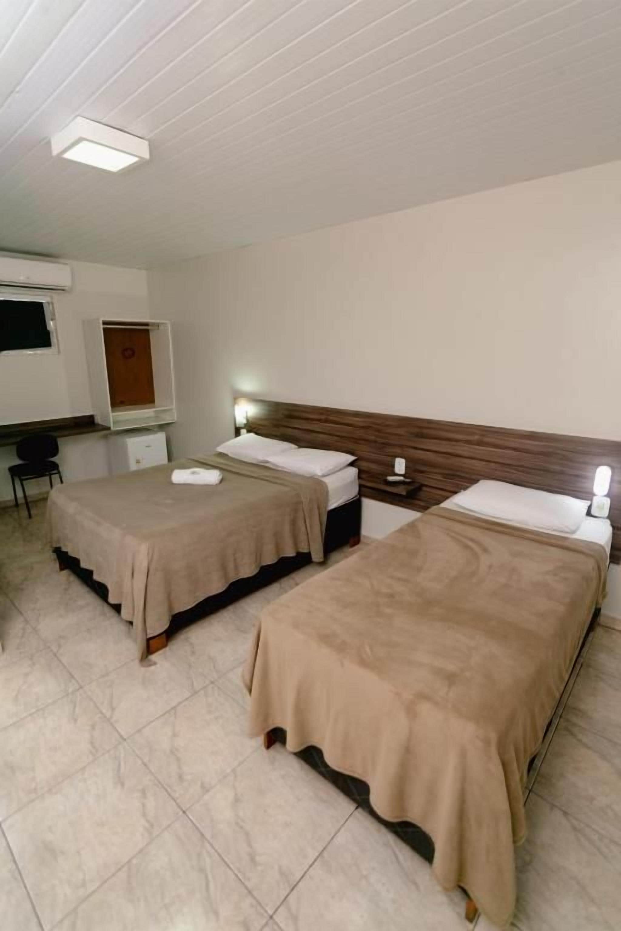 A hotel room with two beds, a desk, and a mirror.