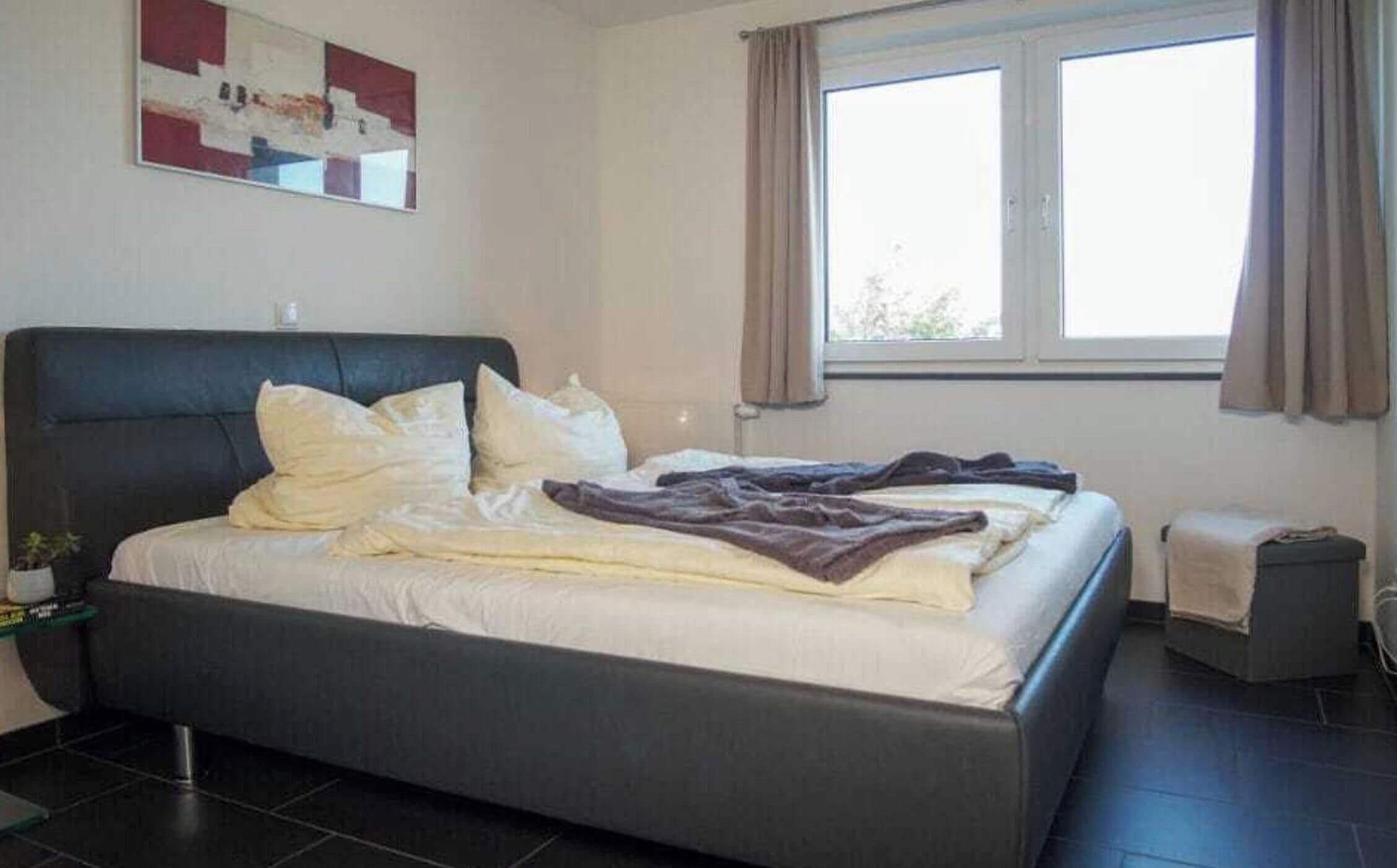 Une chambre à coucher avec un lit, une table de chevet, une fenêtre et un tableau au mur.