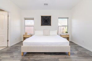 Ein Schlafzimmer mit einem großen Bett, zwei Nachttischen, einem Wandbild und einem Fenster an der Seite.