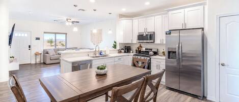 A modern kitchen with white cabinets, stainless steel appliances, and a wooden dining table.