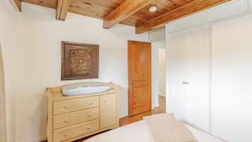 A bedroom with a wooden ceiling, a wooden dresser, a bed with a white blanket, and a white wardrobe.