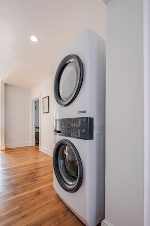 A laundry room with two front-loading washing machines, wooden flooring, and a white wall. - Stylish 2BR apt in beautiful Petersburg w/ parking, laundry, & outdoor space (Petersburg)