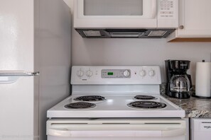 Uma cozinha com fogão branco, micro-ondas em cima e máquina de café no balcão.