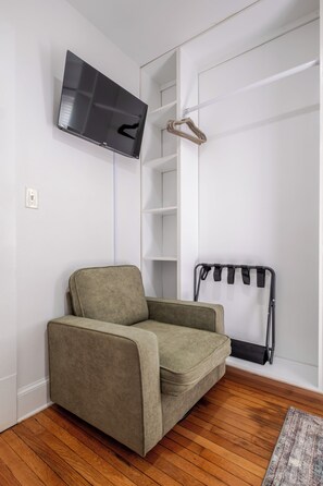 A modern living room with a sofa, a television mounted on the wall, a coat rack, and a wooden floor. - Stylish 2BR apt in beautiful Petersburg w/ parking, laundry, & outdoor space (Petersburg)